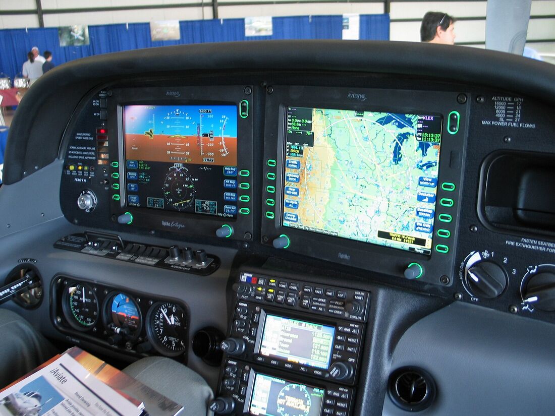The cockpit of a Cirrus SR22 seen from the pilot's seat, with two glass displays lit and paper charts resting below the panel