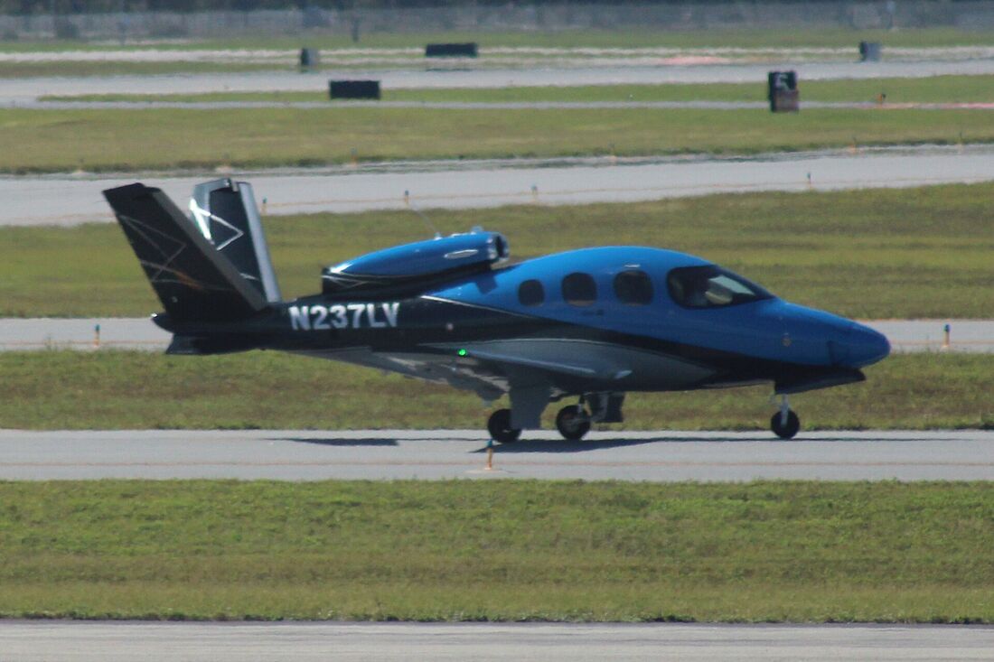 A blue Cirrus SF50 Vision Jet taxiing, showing its V-tail and the single jet engine mounted on top of the rear fuselage